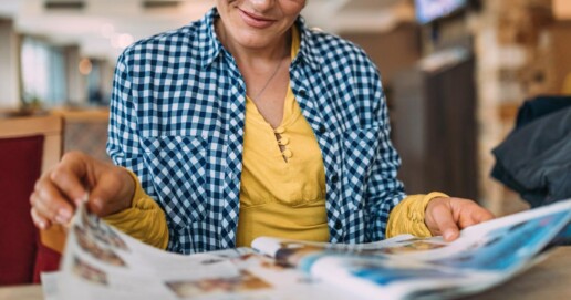Eine Frau sitzt an einem Tisch und blättert in einer Zeitung