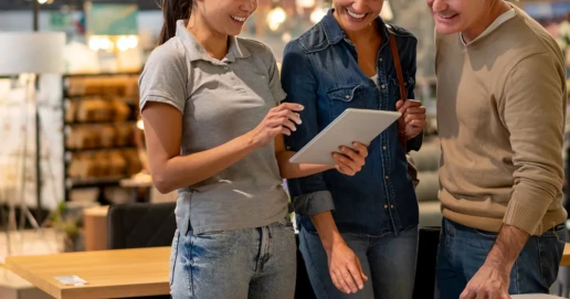 Drei Personen stehen zusammen in einem Geschäft und schauen auf ein Tablet