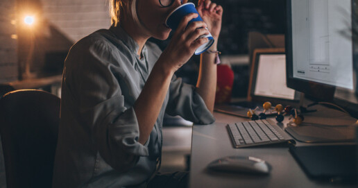 Eine Frau sitzt am PC, arbeitet und trinkt einen Kaffee