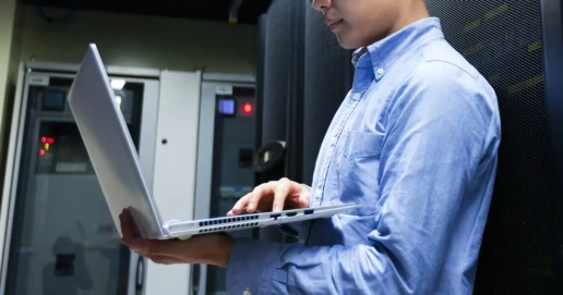 Ein Mann steht mit seinem Laptop auf dem Arm in einen Serverraum